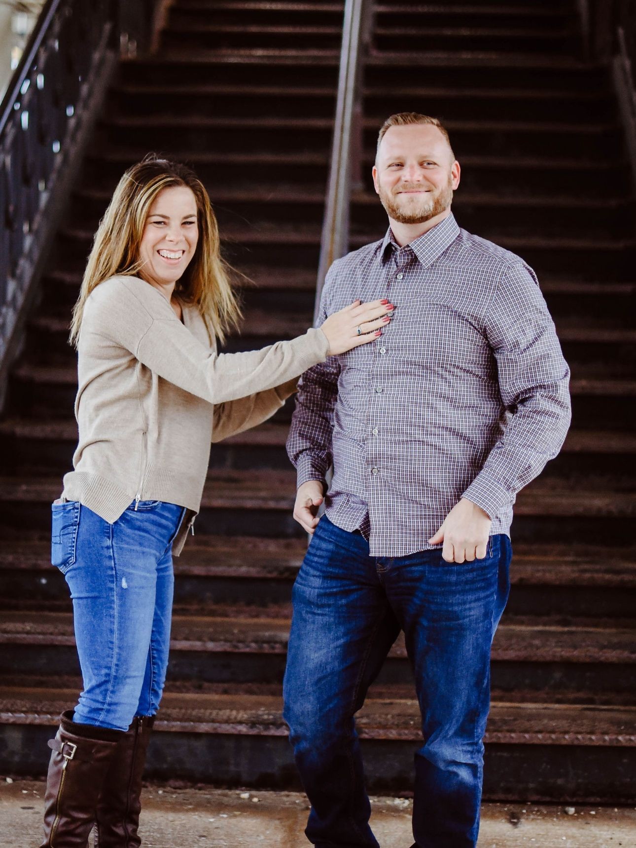 Two people standing on a staircase, the woman adjusting the man's shirt while wearing casual attire.